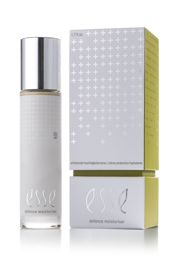 A bottle of Esse Defence Moisturiser with a silver cap stands beside its matching silver and yellow box, both showing modern white plus signs and Esse Defence Moisturiser branding.
