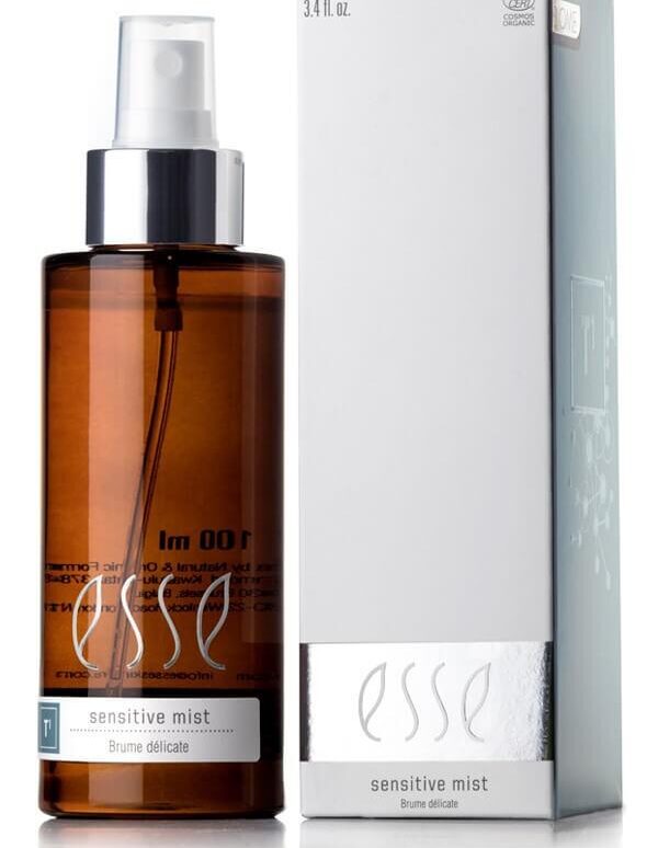 A 100ml brown bottle of "Esse Sensitive Mist," topped with a white spray nozzle, is placed beside a white rectangular box bearing the same product name. The box features a silver band near the bottom and text specifying it as a sensitive mist for delicate skin.